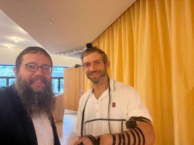 Rabbi Yosef Moscowitz, left smiles with Max after helping him lay tefillin.