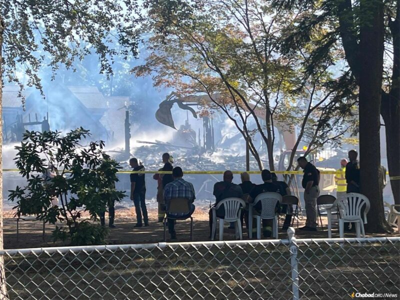 Community members watch emergency-service workers sift through the remains of the synagogue and the home