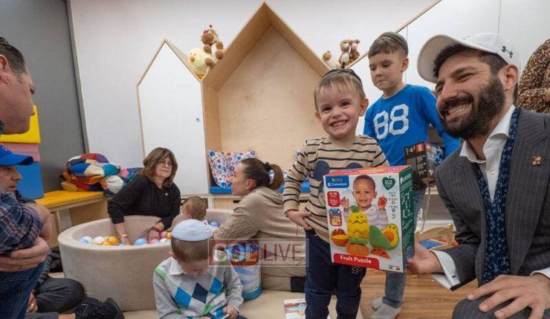 Rabbi JJ Hecht presents gifts to refugees at Chabad of Warsaw, as other members of the delegation play with children. 
